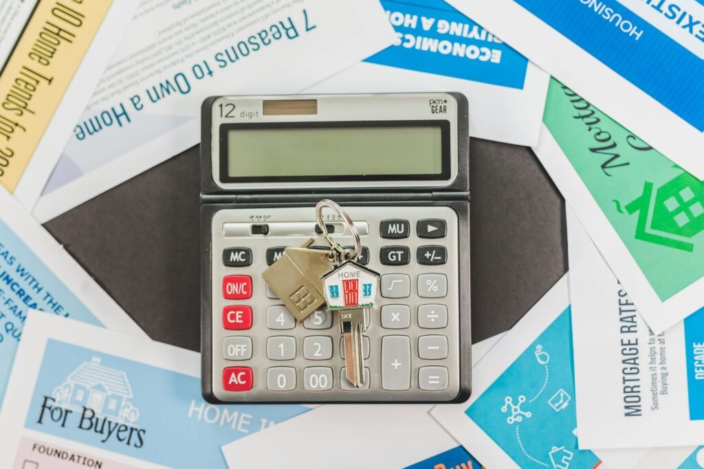 Calculator with a house-shaped keychain surrounded by mortgage and home buying reference materials