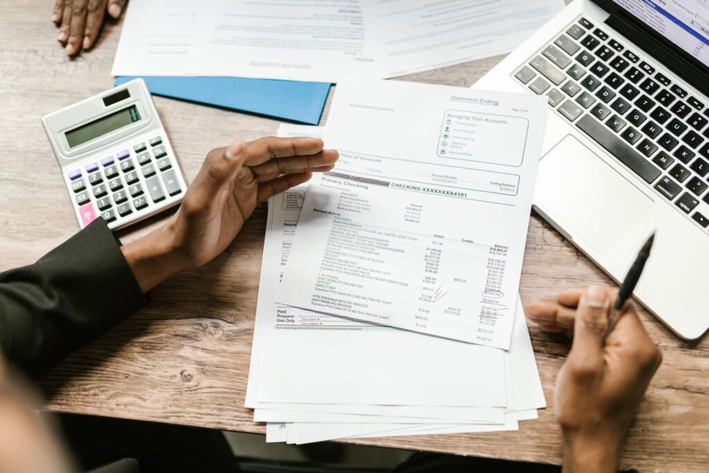Person reviewing a bank statement alongside a calculator and laptop while comparing mortgage bank options