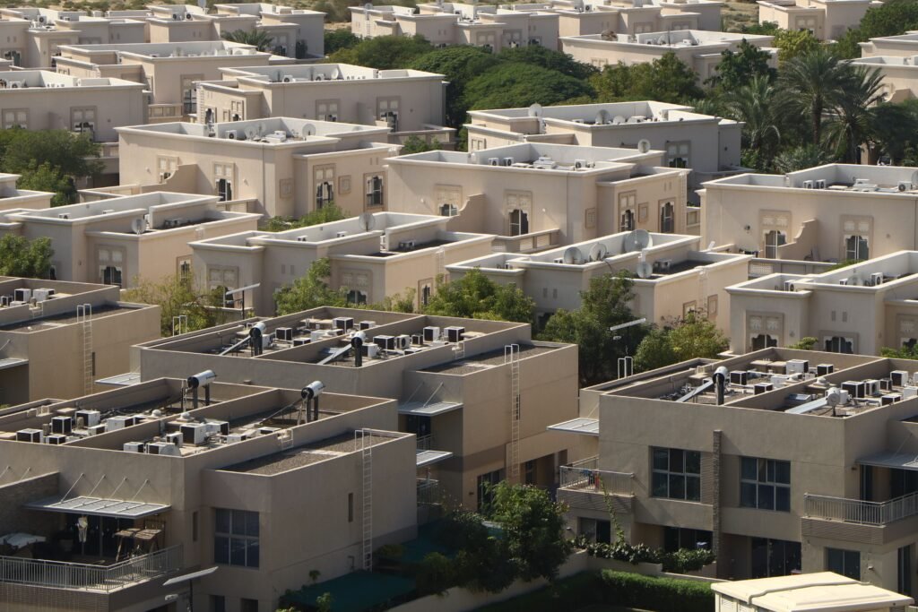 Aerial view of modern residential townhouses and villas in a Dubai community showing cream-colored facades, flat roofs, and landscaped courtyards