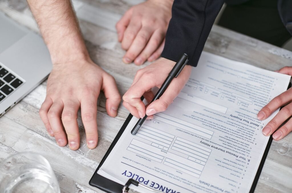 Two people reviewing and signing an insurance policy document on a wooden desk, close-up of hands and pen