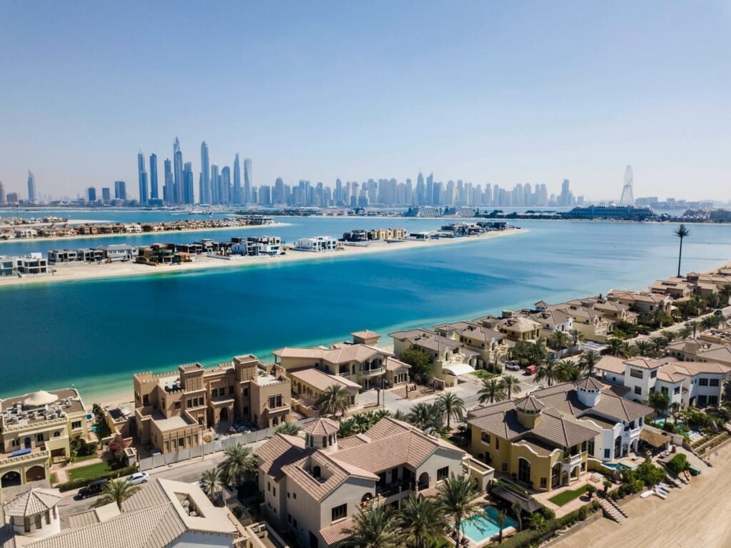 Aerial view of a Dubai waterfront villa community on a palm-frond island with the Dubai Marina skyline in the background