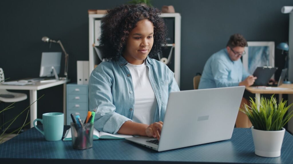 Young professional working on a laptop at her desk in a modern office, representing starting a new job