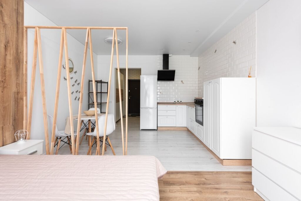 Bright open-plan studio apartment with a bed, dining table behind a wooden partition and a white kitchen, the kind of small unit a buyer finances under AED 1 million
