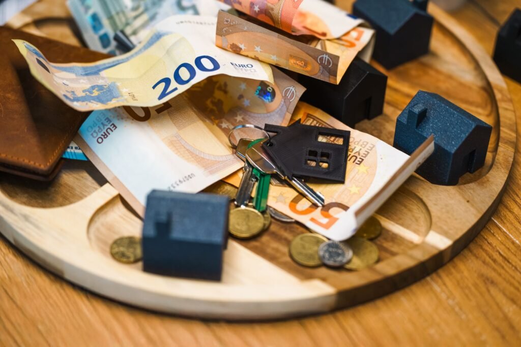 Euro banknotes, coins and house-shaped keychain with miniature houses on a wooden tray, symbolising financing a Dubai property purchase from the eurozone