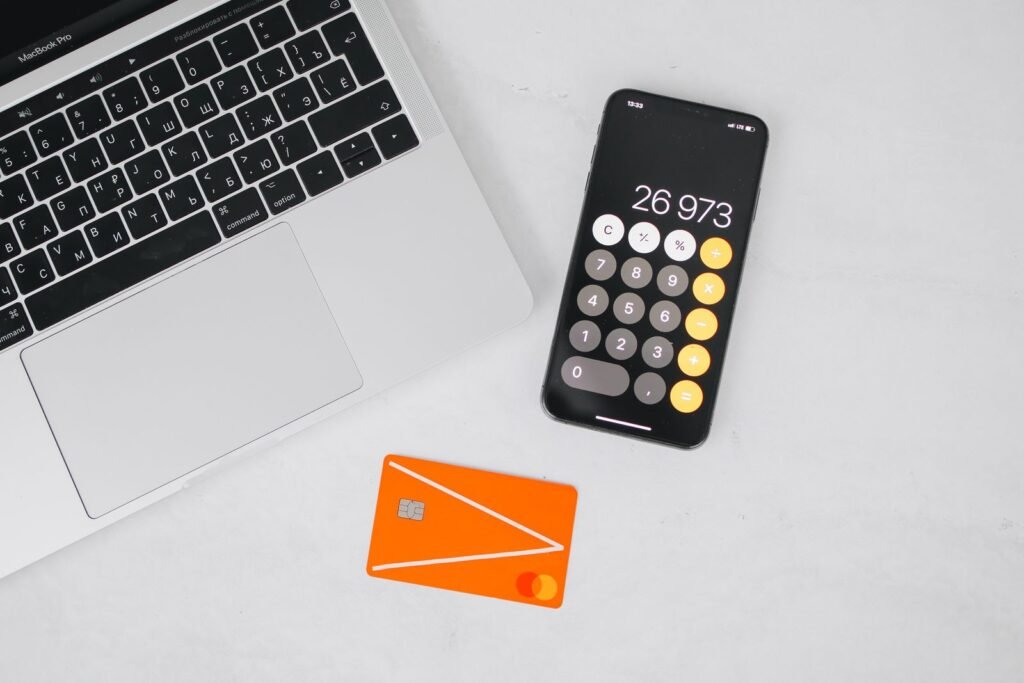 Laptop, smartphone showing a calculator and an orange credit card on a white desk, the debts and monthly payments a bank adds up before approving a UAE mortgage