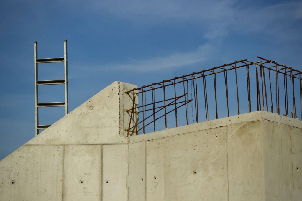 Concrete walls of a building under construction with exposed steel rebar and an aluminium ladder against a clear blue sky, representing staged construction finance for a self-build villa in the UAE