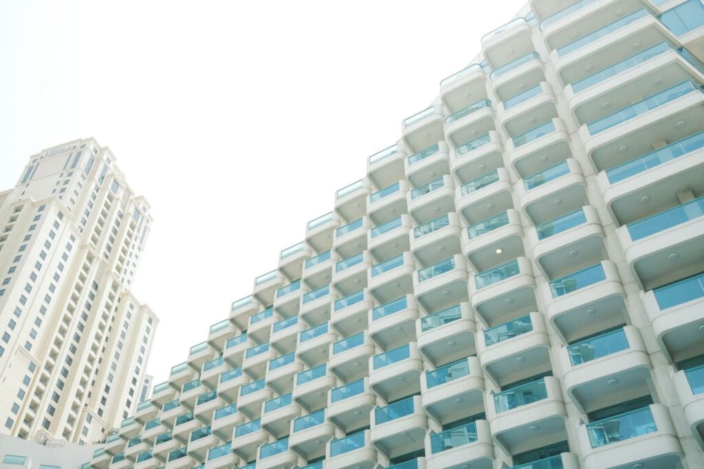 Low-angle view of a white high-rise apartment block with glass balconies beside a residential tower in Dubai, illustrating the rent or buy in Dubai decision