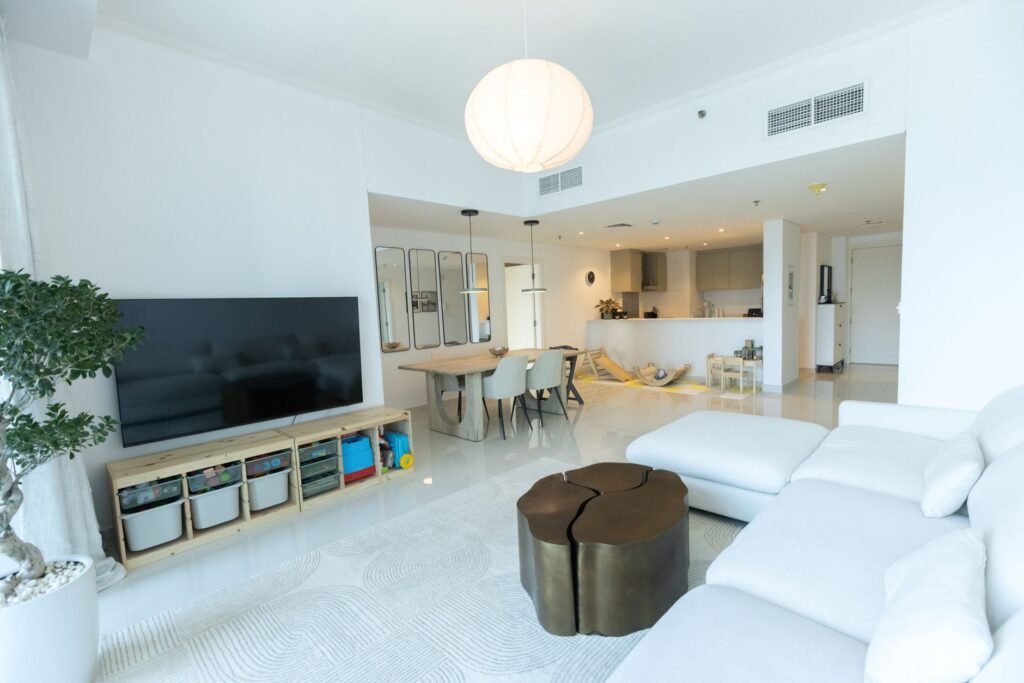 Furnished, lived-in Dubai apartment living room with a white sofa, dining table and open kitchen, the kind of home a buyer inherits with a tenant inside