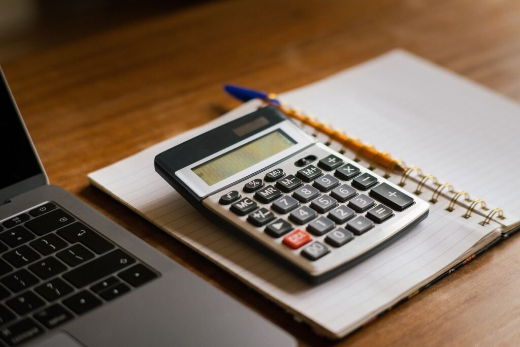 Calculator resting on an open spiral notebook beside a laptop on a wooden desk, representing mortgage payment calculations